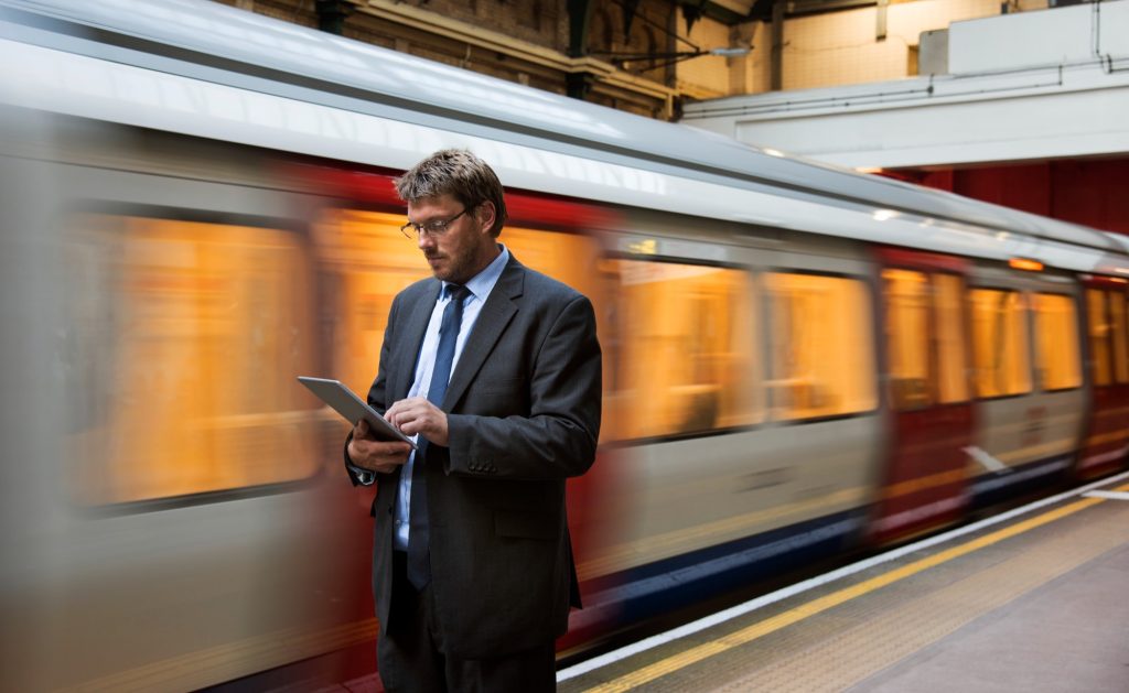 A man on a suit holding a tablet at the train station