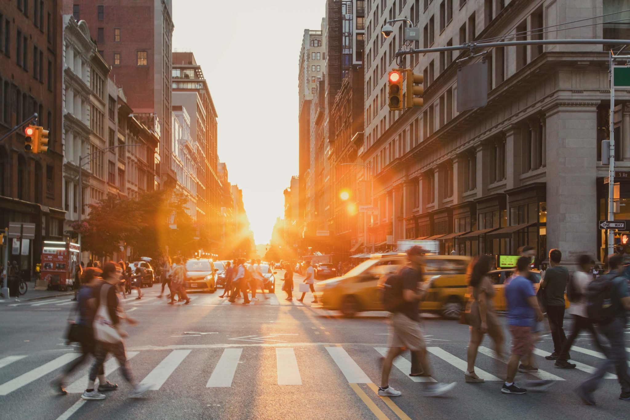 Busy intersection is crowded with people and cars on 5th Avenue and 23rd Street in New York City with sunset background